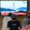 People watch a television screen showing a news broadcast with file footage of a North Korean satellite-carrying rocket launch, at a railway station in Seoul in August 2023