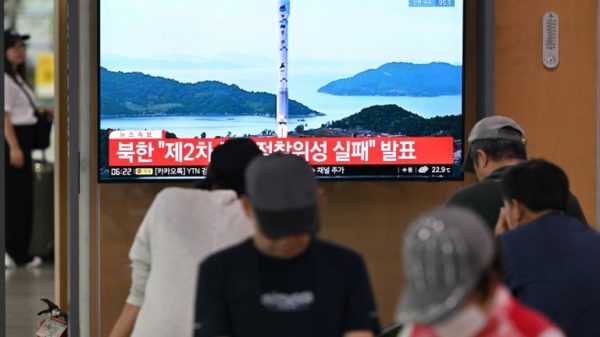 People watch a television screen showing a news broadcast with file footage of a North Korean satellite-carrying rocket launch, at a railway station in Seoul in August 2023