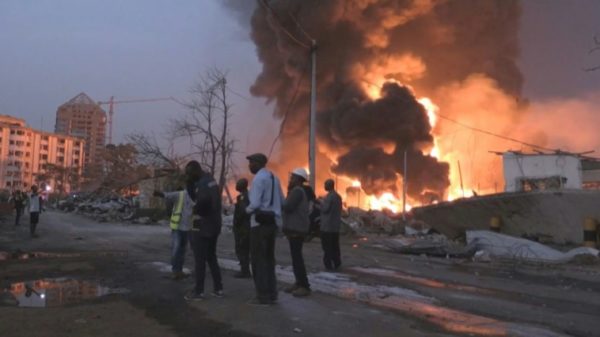 People are seen in front of flames from the fire at Conakry's main fuel depot on December 18, 2023