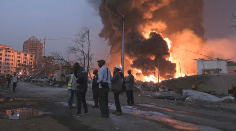 People are seen in front of flames from the fire at Conakry's main fuel depot on December 18, 2023