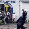 A police officer throws a rock at opposition supporters outside their party HQ in Kinshasa