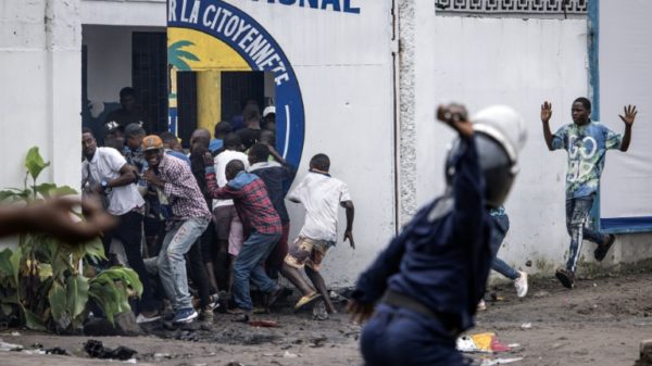 A police officer throws a rock at opposition supporters outside their party HQ in Kinshasa