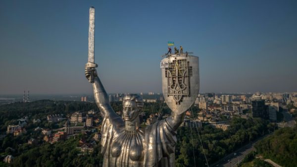 Steeplejacks wave the Ukrainian flag after finishing installing the coat of arms of Ukraine on the shield of the 62 metre Motherland Monument in Kyiv