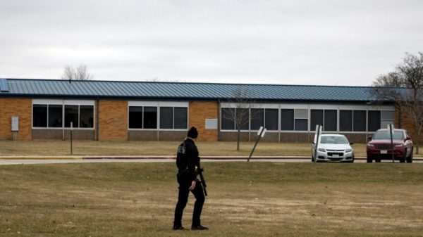 An armed police officer walks the perimeter of the Perry High School in Iowa after a shooting