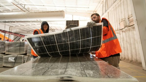 Workers push damaged solar panels into a machine to be recycled at the We Recycle Solar plant in Yuma, Arizona