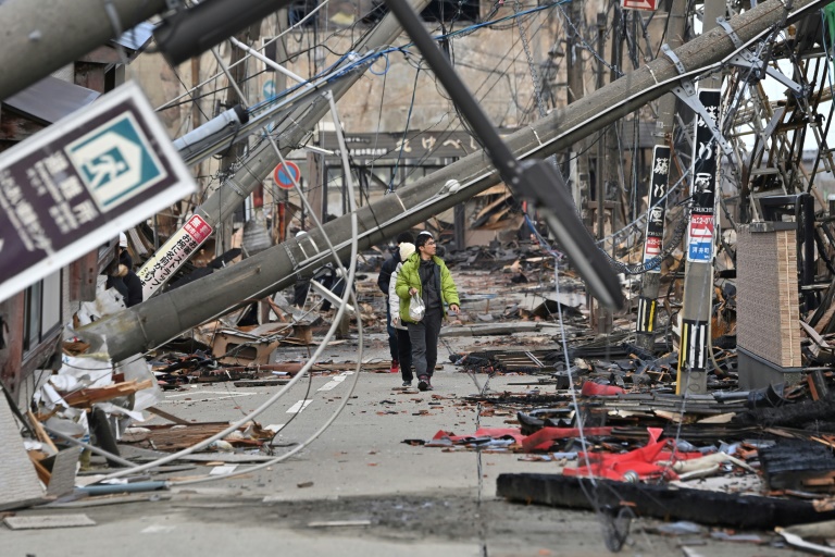 People walk past fallen utility poles and damaged buildings in the city of Wajima, Ishikawa prefecture