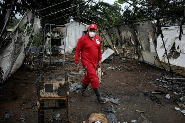 A Red Cross worker walks around a burnt-out tent that was set alight by migrants angry that they&apo...