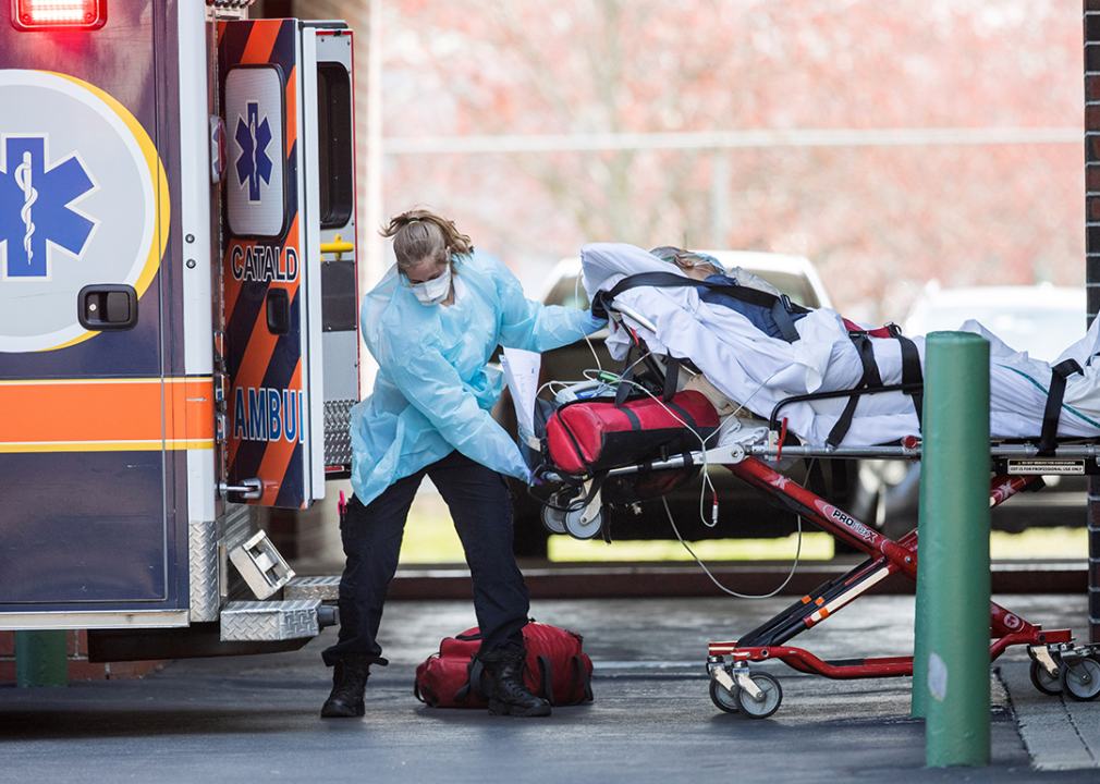 A first responder wearing a face mask loads a patient into an ambulance.