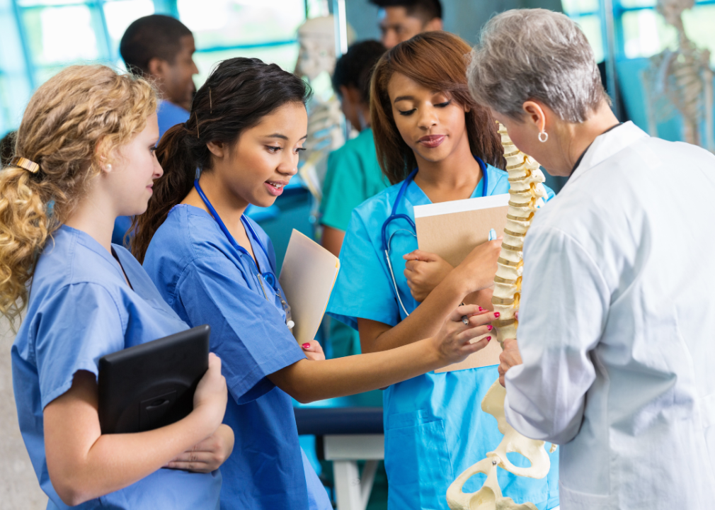 Three nursing students looking at a model of a spine.