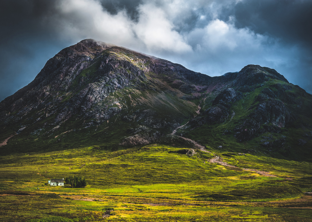 Tall mountains surrounding small white house in green valley.  